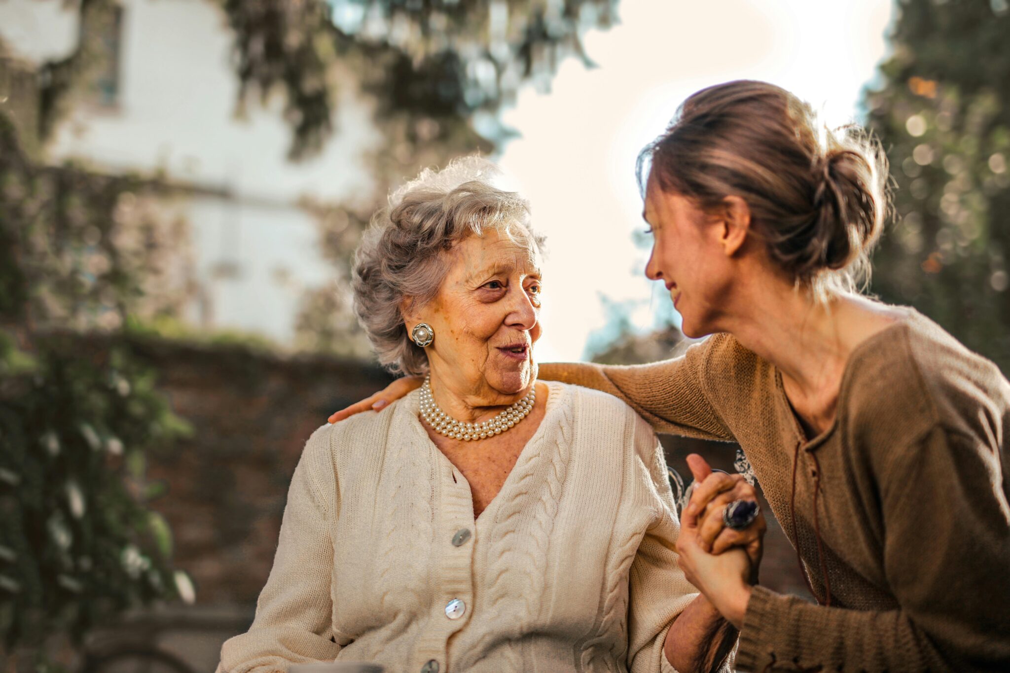 Elderly woman and https://raghunathelderscare.org/https://raghunathelderscare.org/adult daughter share a joyful, affectionate moment in a sunny garden.