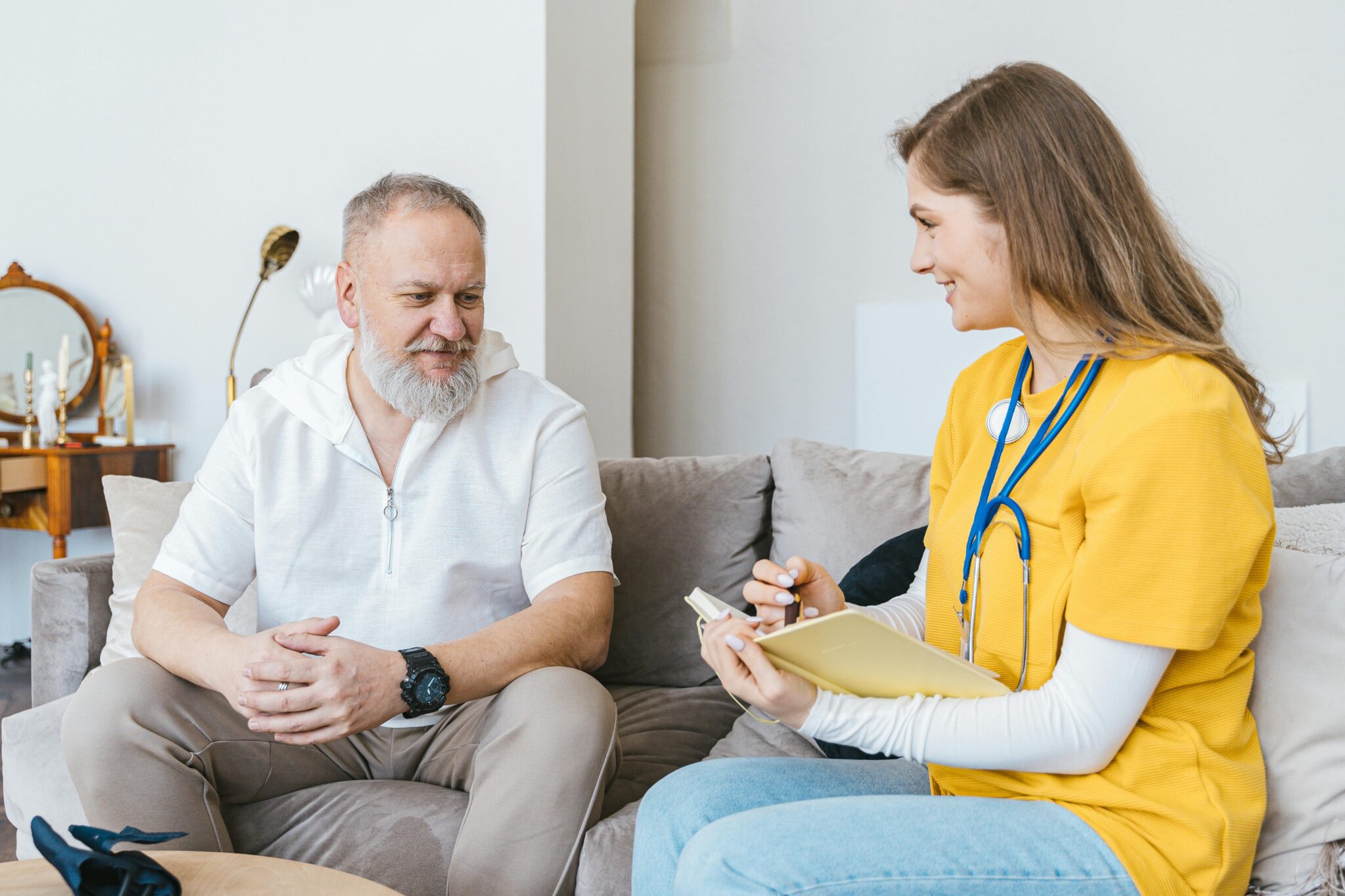 A healthcare professional smiles while consulting with an elderly man in a cozy indoor setting.